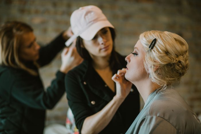 Bridemaid having make up done by a make up artists wearing a light pink baseball cap